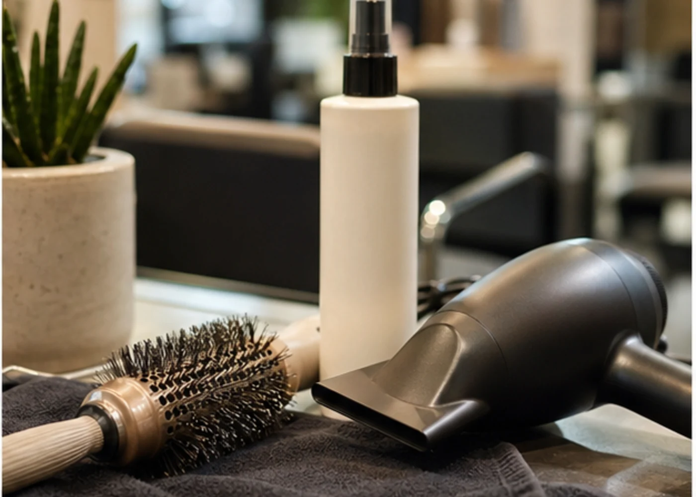 Round brush, blow dryer, towel, and unbranded heat styling bottle on a salon station.